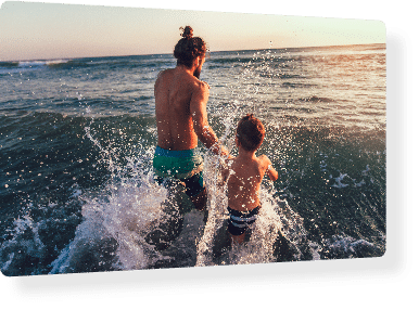 Mann und Kind spielen im Meer bei Sonnenuntergang.